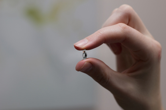 An Earlens custom lens resting between a woman's thumb and forefinger