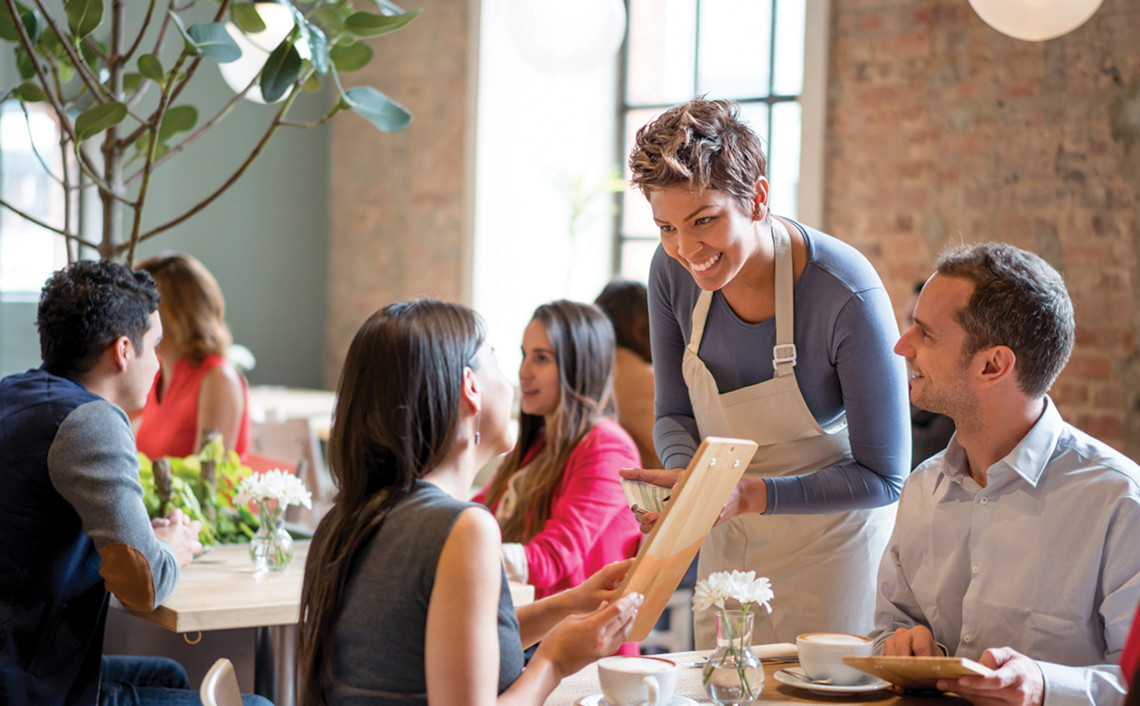 A man and woman easily converse with a waitress at a restaurant